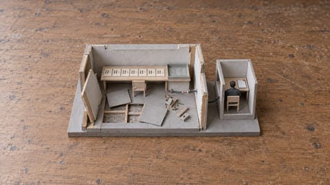 A handmade model of a dismantled room contains seven matching score cards and an empty file tray, with a cable leading to a separate reviewer booth.